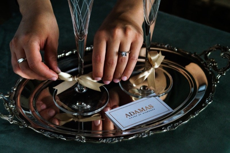 Hands tying ribbons on champagne glasses on a silver tray