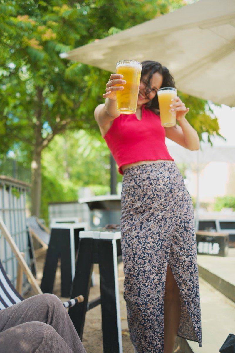 Woman holding up two drinks at an outdoor bar